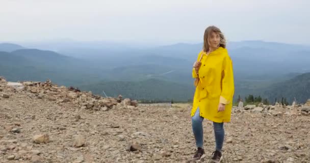 Randonneuse femme marchant avec sac à dos en imperméable jaune dans les montagnes — Video