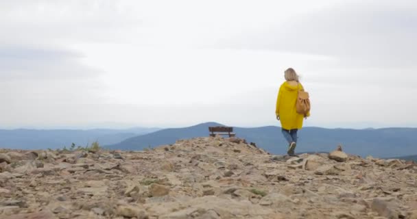 Caminante mujer caminando con mochila en impermeable amarillo en las montañas — Vídeo de stock