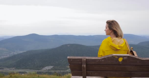 Egy sárga esőkabátot lány ül a tetején egy hegy, élvezi a csodálatos kilátás — Stock videók