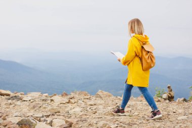 Harita arıyorum hipster genç kız dağ, tepe üzerinde sırt çantası ile sarı yağmurluk. Arka plan Vadisi manzara görünümü mockup üzerinde turist gezgin
