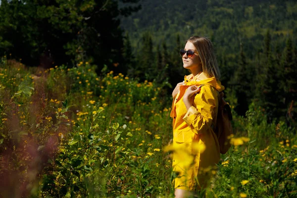 Bokovky mladá dívka v žlutá pláštěnka s batohem na vrchol hory. Turistické cestovatel na pozadí — Stock fotografie