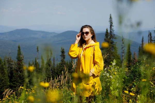 Mulher hipster elegante em viajante capa de chuva amarela com mochila no topo das montanhas, conceito de viagem, viajar de pé na montanha . — Fotografia de Stock