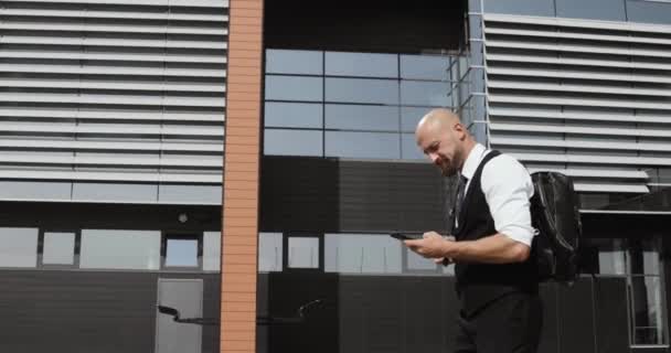 Бизнесмен гуляет по улицам делового района и пользуется мобильным телефоном — стоковое видео