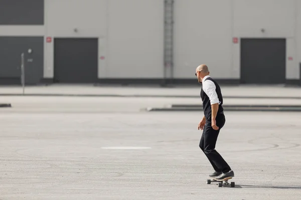 Jovem na moda belo terno no skatebourd longboard no aeroporto perto do edifício moderno — Fotografia de Stock