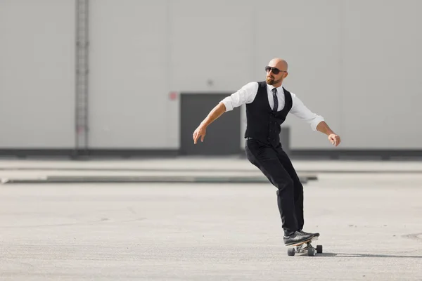 Ung man på mode fin dräkten på den longboard skatebourd på flygplatsen nära modern byggnad — Stockfoto