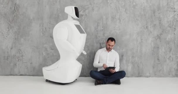 Ένα κομψό άνδρα επικοινωνεί με ένα ρομπότ, πιέζει ένα πλαστικό μηχανικό βραχίονα για το ρομπότ, χειραψία. Κυβερνητικό σύστημα σήμερα. Σύγχρονη ρομποτικές τεχνολογίες. Αυτόνομο ρομπότ humanoid. — Αρχείο Βίντεο