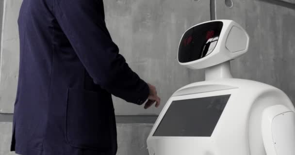 Ein stilvoller Mann kommuniziert mit einem Roboter, drückt einen mechanischen Plastikarm an den Roboter, Handschlag. kybernetisches System heute. moderne Robotertechnologien. Humanoider autonomer Roboter. — Stockvideo