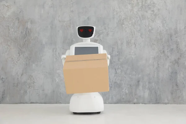 Humanoid autonomous robot with cardboard box in hand on grey background. the robot delivers the parcel. delivery concept. — Stock Photo, Image