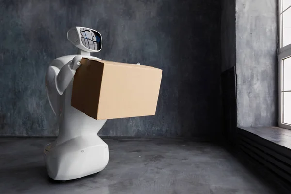 Humanoid autonomous robot with cardboard box in hand on grey background. the robot delivers the parcel. delivery concept. — Stock Photo, Image