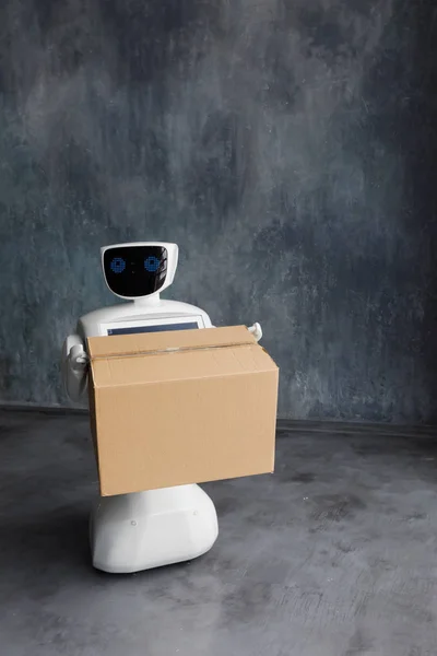 Humanoid autonomous robot with cardboard box in hand on grey background. the robot delivers the parcel. delivery concept. — Stock Photo, Image