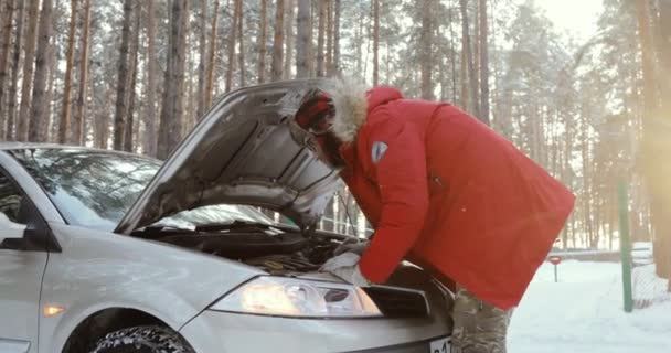 Mann schaut auf Motor des Autos. Mann repariert kaputtes Auto. Wintereinbruch, Ärger auf schneeglatter Landstraße. — Stockvideo