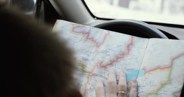 Ember kezében autóvezetés, keres egy papír térképet irányban. Felismerhetetlen férfi vezető kezében tartja a kormánykeréken, navigáció esik, táj, és erdő. téli vezetés — Stock videók