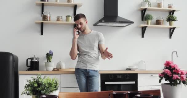 Kaukaski mężczyzna pobyt na kuchnię i rozmawia przez telefon w domu. — Wideo stockowe