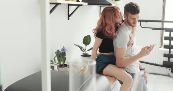 Atractiva pareja joven con teléfono inteligente en casa en la cocina — Vídeo de stock