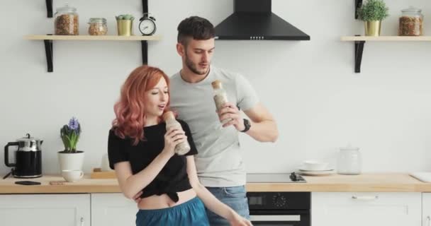 Утро дома счастливая молодая пара молодожёны танцуют, слушая музыку на кухне в пижаме в любви весело — стоковое видео
