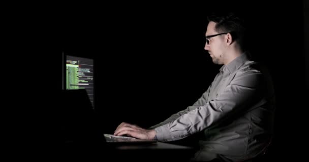 Программист работает с кодом на экране в офисе сверхурочно поздно ночью сидя перед двумя мониторами . — стоковое видео