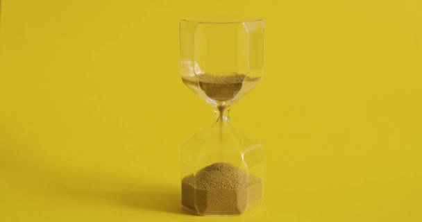 Zandloper op gele achtergrond. Tijd is. Tijd-en vergankelijkheid concept. — Stockvideo