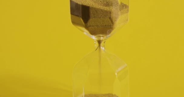 Reloj de arena sobre fondo amarillo. La arena se vierte de una parte a otra. Concepto de tiempo y transitoriedad . — Vídeo de stock