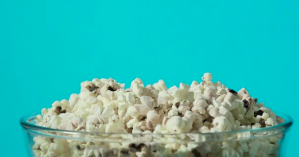 Mans mano está tomando palomitas de maíz fresco sabroso de tazón de vidrio transparente sobre fondo azul . — Vídeo de stock