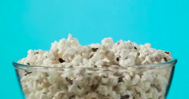 Rotating glass bowl with fresh popcorn on blue background. — Stock Video