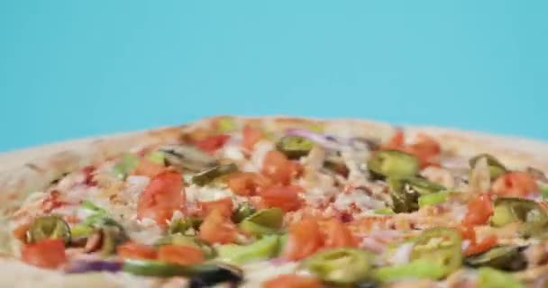 Close-up view of rotating tasty pizza with bacon and vegelables on blue background. — Stock Video