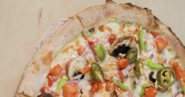 Close-up weergave van roterende half smakelijke pizza met spek en groenten op licht houten achtergrond. Verticaal scherm voor mobiele apparaten. — Stockvideo