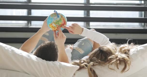 Couple in love in bed are looking at globe choosing a place to travel on honeymoon. — Stock Video