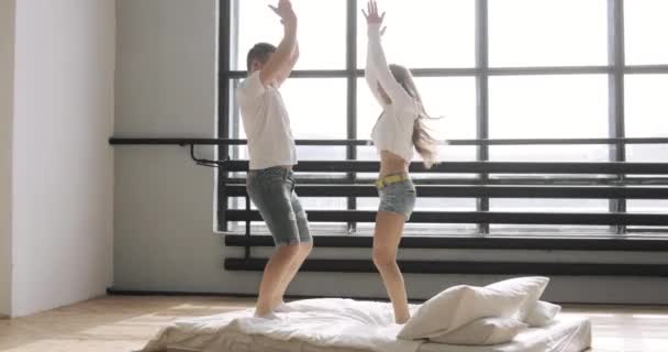 Feliz pareja joven están saltando en la cama aplaudiendo y tomados de la mano. Concepto de relación . — Vídeo de stock