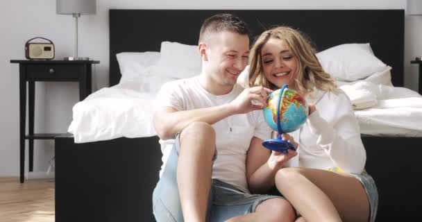 Couple amoureux assis à côté du lit regardent globe choisir un endroit pour voyager en lune de miel . — Video