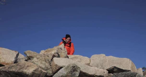 Il giovane escursionista è felice della sua salita in cima alla scogliera. Il vincitore sta alzando le mani sullo sfondo del cielo . — Video Stock