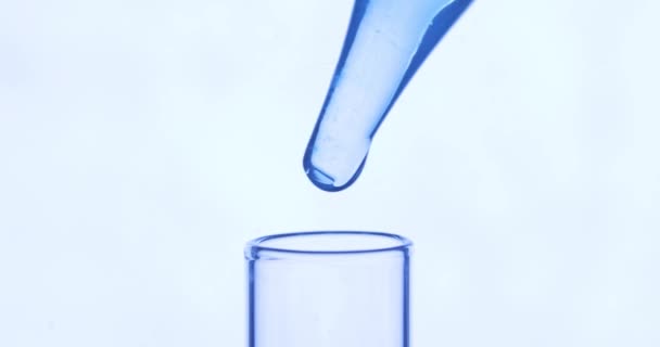 Pipetta csöpög átlátszó kék vegyi anyagok kémcsőbe, fehér alapon. Kémiai és gyógyászati koncepció. — Stock videók