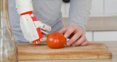 Robotik protez el ile adam üzerinde bıçak ahşap tahta üzerinde domates kesiyor. Kas reennervation teknolojisi.