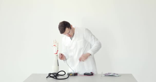 Scientist engineer connects and configures robotic prosthesis hand on the table on white background. — Stock Video
