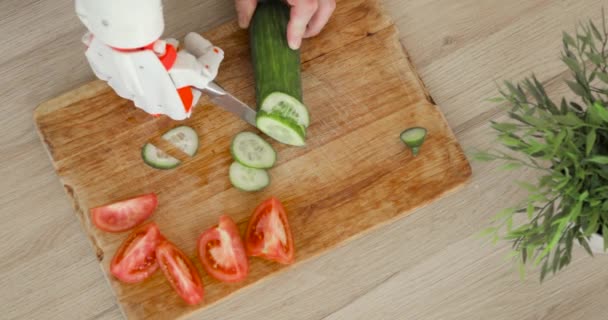 Man met robot protheses hand met mes op het probeert te snijden komkommer voor salade op houten bord. Muscle reinnervation technologie. — Stockvideo