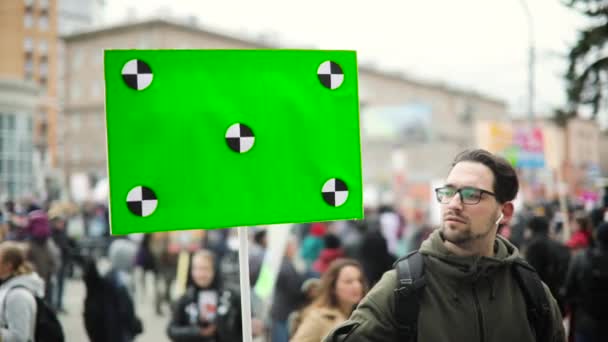 Young man is looking at poster with green screen in his hand on city demonstration. — Stock Video