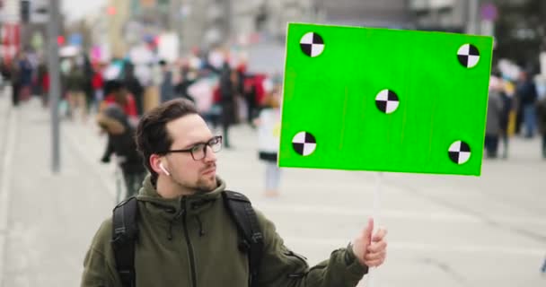 Mladý muž se dívá na plakát se zelenou obrazovkou v ruce na městském shromáždění. — Stock video