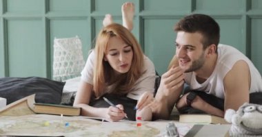 Çift erkek ve kadın bir dünya haritası kullanarak tatil planlıyoruz. Tartışma noktalarını not eden kadın yatakta yatıyordu.