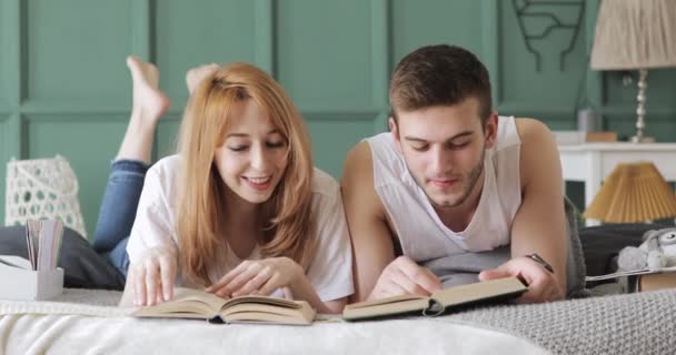 Menina e cara estão lendo um livro juntos em voz alta deitado na cama . — Vídeo de Stock