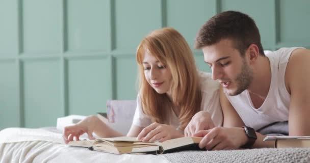 Menina e cara estão lendo um livro juntos deitado na cama . — Vídeo de Stock