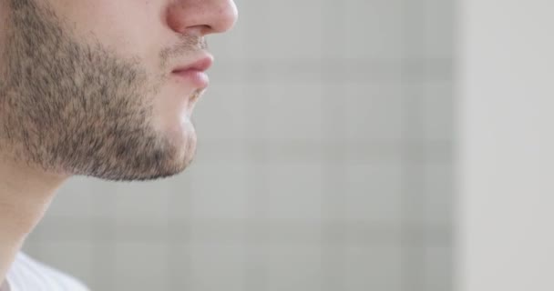 Young man is eating burger at home, face closeup, side view. — 图库视频影像