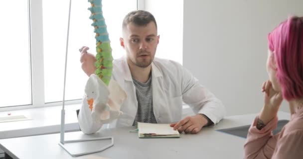 Hombre médico está explicando plan de tratamiento a paciente usando modelo de columna vertebral . — Vídeo de stock