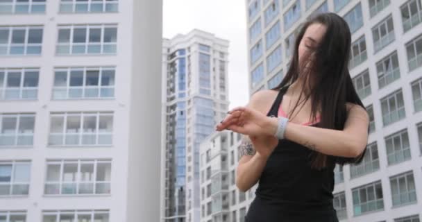 Jovem mulher configura relógio inteligente antes de correr e vai correr no distrito da cidade . — Vídeo de Stock