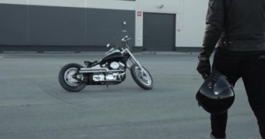 Genç adam bisikletçi motosikletine gider ve üzerine oturur.