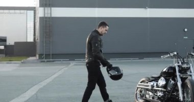 Genç adam motorcu motosikletine gider, kaskını giyer ve üzerine oturur..