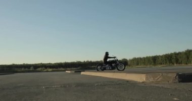 Biker hızla gün batımında orman yakınında yolda bir motosiklet sürmek, yan görünüm.