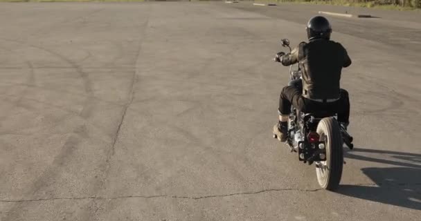 Man Biker rijdt een motorfiets op de weg in de stad bij zonsondergang, achteraanzicht. — Stockvideo