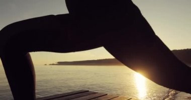 Gün batımında Warrior I Pose yoga nehir iskelesinde Kadın, yan görünüm.