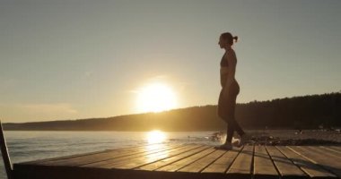 Gün batımında nehir iskelesinde Warrior I Pose yoga kadın siluet.