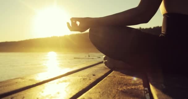 Žena medituje v lotosové pozici na řece drží ruce v Namaste mudru při západu slunce.