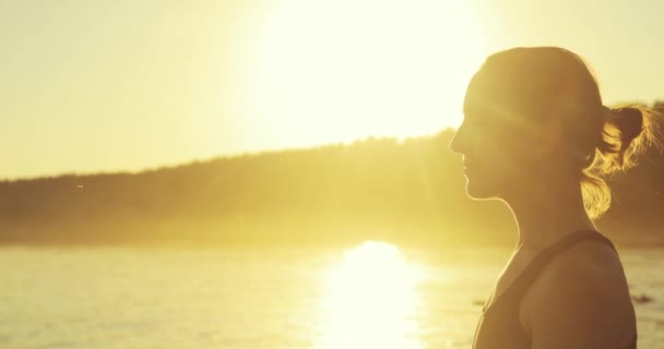 La mujer está meditando en posición de Loto en el muelle del río al atardecer amarillo, vista lateral . — Vídeo de stock